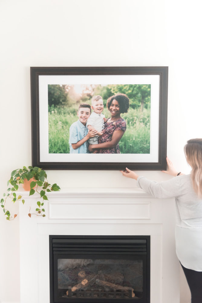 woman hanging portrait of three children over fireplace